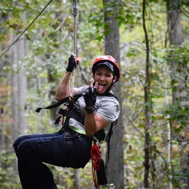 Happy woman ziplining through a forest, smiling and throwing a peace sign