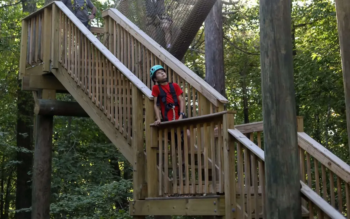 Child wearing a helmet and harness looking up from a zipline platform on a treetop adventure course in Tennessee