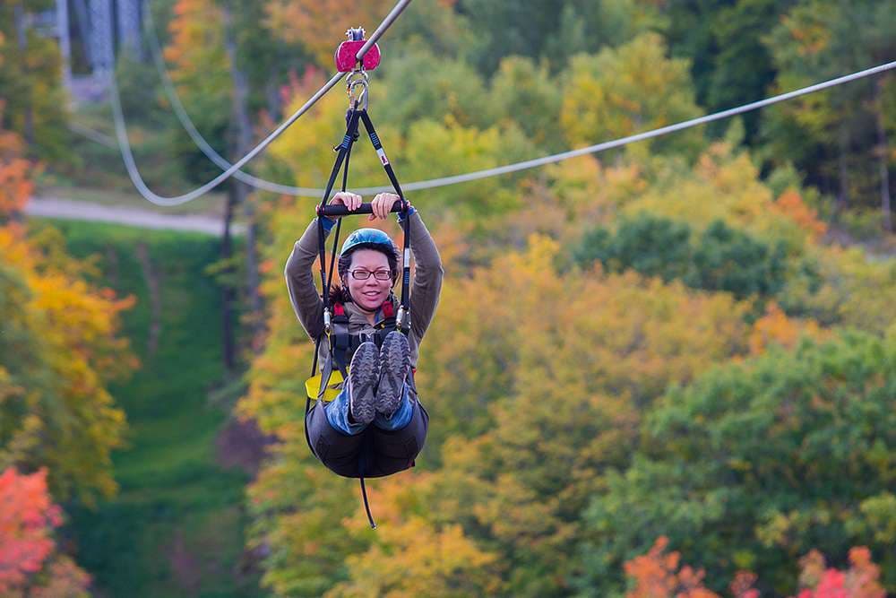 Smiling guest in a helmet and harness zipping high above a canopy of autumn trees